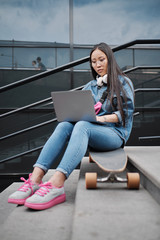 Fototapeta na wymiar Teenager in glasses sitting on the longboard outside with a laptop.