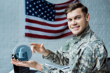 happy military man gesturing in office near virtual padlock and laptop