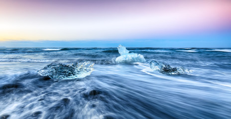 Incredible pieces of the iceberg sparkle on famous Diamond Beach at  Jokulsarlon lagoon during sunset