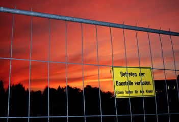 Bauzaun mit Warnschild Eltern haften für ihre Kinder vor dramatischem Sonnenuntergang