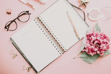 Fashion blog, home office desk. Female workspace with laptop, pink hydrangea, golden accessories, pink diary on pink background. Top view. Copy space. Toned images