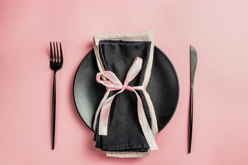 Elegant black and pink table setting: plates, napkin and silverware. Flat lay. Pink background
