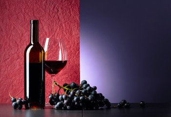 Bottle and glass of red wine on a black table.