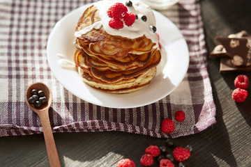 Image of delicious breackfast for family, pancackes with sour cream and fresh berries, muffins decorated with raspberries, blueberries, wooden spoon, white palte on dark table. Food concept.