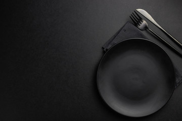 Elegant black table setting: plates, napkin and silverware over black background. Flat lay. copy...