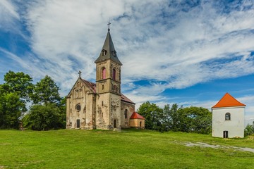 Fototapeta na wymiar Krasikov, Kokasice / Czech Republic - August 9 2019: View of the church of Mary Magdalene and a bell tower. Bright sunny summer day with blue sky and white clouds, green grass and trees.