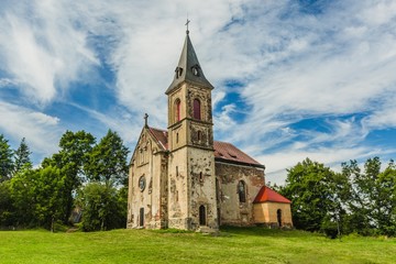 Fototapeta na wymiar Krasikov, Kokasice / Czech Republic - August 9 2019: View of the old church of Mary Magdalene. Bright sunny summer day with blue sky and white clouds, green grass and trees.