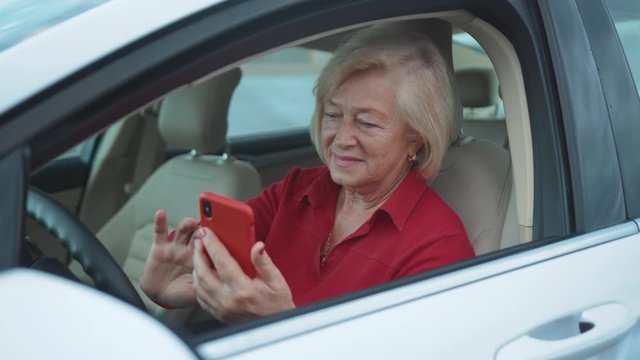 Close up senior woman sits in car uses red cell phone smile happy businesswoman blonde people smartphone cellphone communication internet search lady mobile bench browse network online slow motion