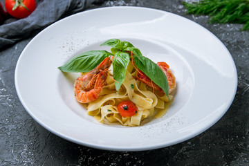Pasta fettuccine with shrimps, tomatoes and basil on grey concrete background