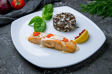 Salmon steak on the grill with red caviar and black rice on grey concrete background