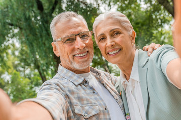 Loving senior couple embracing and taking a selfie on mobile phone outdoors