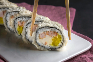 Sushi roll with chopsticks on a white plate close up. Pink napkin on a gray background