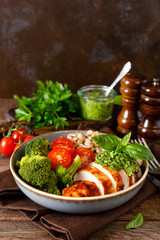 Chicken lunch bowl with broccoli, fresh tomato, pearl barley porridge and basil pesto on wooden rustic background