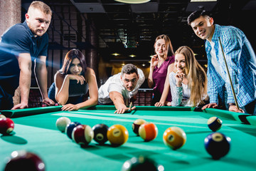 Group of young cheerful friends playing billiards.