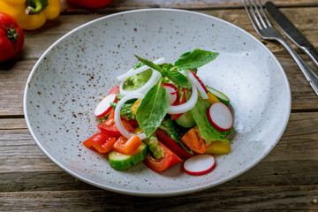 Vegetable salad with tomatoes and cucumbers and onion on old wooden table