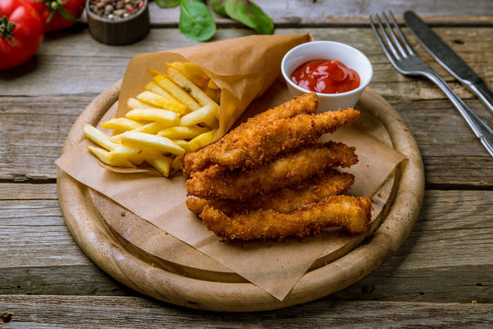 Chicken strips with ketchup and french fries on old wooden table