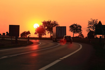 Samochód osobowy i ciężarowy, tir na tle zachodzącego słońca, droga ekspresowa.
