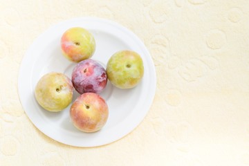 ripe plums in a white plate on a table with a yellow tablecloth