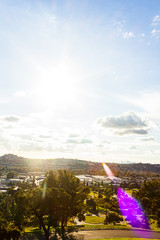 sunflare over panaramic city view with hillsides and trees, homes, businesses