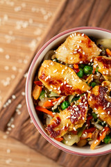 Sweet and sour asian chicken. Asian bowl with chicken and vegetables on bamboo background. Top view.