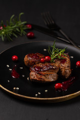 Venison or deer steak with ingredients like sea salt, rosemary and cranberry on black plate. Food background for restaurant.