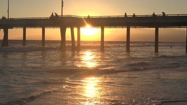 Silhouetted tourists walk on a pier during a beautiful golden sunset