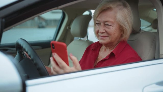Portrait senior woman sits in car use red cell phone smile happy businesswoman blonde people smartphone cellphone communication internet search lady mobile bench browse network online slow motion