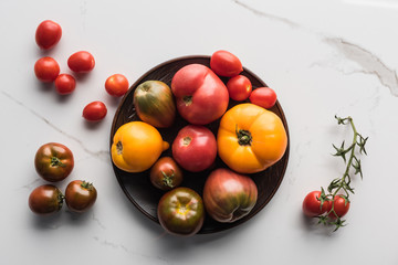 top view of tomatoes on wooden plate near scattered tomatoes on marble surface