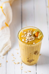 Mango smoothies, yellow fruit juice on white wooden background. Refreshing mango smothie served with oat flakes and physalis.