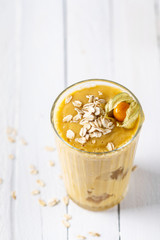 Mango smoothies, yellow fruit juice on white wooden background. Refreshing mango smothie served with oat flakes and physalis.