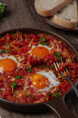 Shakshuka, fried eggs in tomato sauce in pan on wooden background.