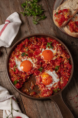 Shakshuka, fried eggs in tomato sauce in pan on wooden background. Top view