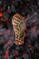 Fried meat steak on a black background of charcoal. Cooked juicy steak with smoke on the coals with...