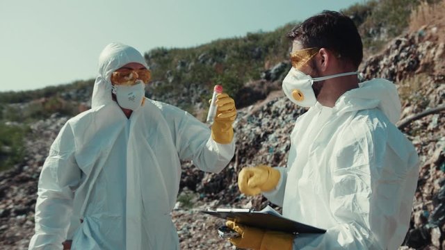 Biological hazard. Scientists team analyzing pollution on waste dump. Close-up two ecologists examining toxic liquids in test tubes.