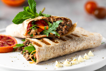 Tortilla wraps sandwiches with fresh vegetables, minced meat and blood oranges on plate. Burrito, sandwich wrap, fajita wrap