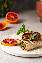 Tortilla wraps sandwiches with fresh vegetables, minced meat and blood oranges on plate. Burrito, sandwich wrap, fajita wrap