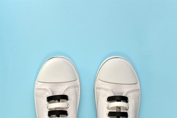 White athletic shoes with striped silicone lace-up closures. The visible front half of the shoes is parallel to each other in the distance. On a blue background from below.