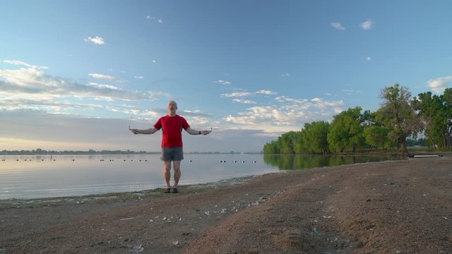 Senior man is exercising with a heavy  fitness jump rope on a sandy lake beach - summer morning in Boyd Lake State Park in northern Colorado