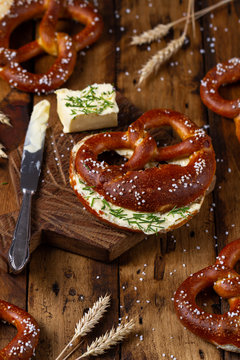 Freshly baked homemade soft Brezel with salt, butter and chive on rustic wooden table. German pretzel called Brezel.
