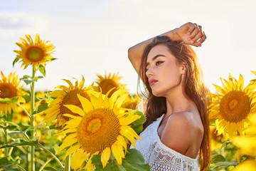 Beautiful young girl enjoying nature on a field of sunflowers. Sunlight plays on the field. Outdoor lifestyle. Summer cozy mood.