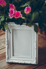 White photo frame on a table with a bouquet of roses. Pink roses and photo frame.