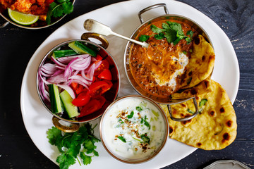 Indian curry meal with black lentils dal, salad, naan bread and raita