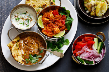 Indian curry meal with black lentils dal, spicy potatoes, rice, naan bread and raita