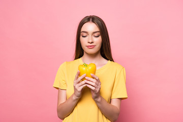 front view of attractive young woman in t-shirt holding yellow bell pepper on pink