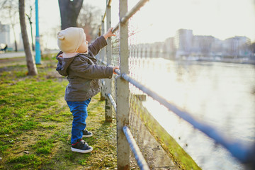 One year old girl standing next to metal fence in park