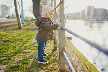 One year old girl standing next to metal fence in park