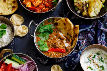 Indian curry meal with black lentils dal, spicy potatoes, rice, naan bread and raita