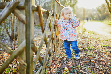 One year old girl standing next to wooden fence in park