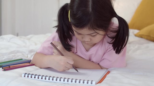 Young Asian girl drawing at home. Asia japanese woman child kid relax rest fun happy draw cartoon in sketchbook before sleep lying on bed, comfort and calm in bedroom at night concept. Slow motion.