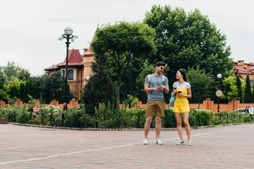 Obraz premium handsome man and asian woman smiling and holding paper cups